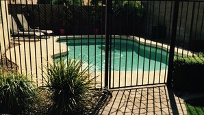 Ein Garten mit Swimmingpool, umgeben von einer Ziegelterrasse und einem Metallzaun.