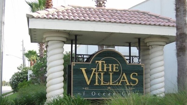 Señalización para 'The Villas of Ocean Gate' con un diseño tradicional, sobre un fondo verde y letras doradas.