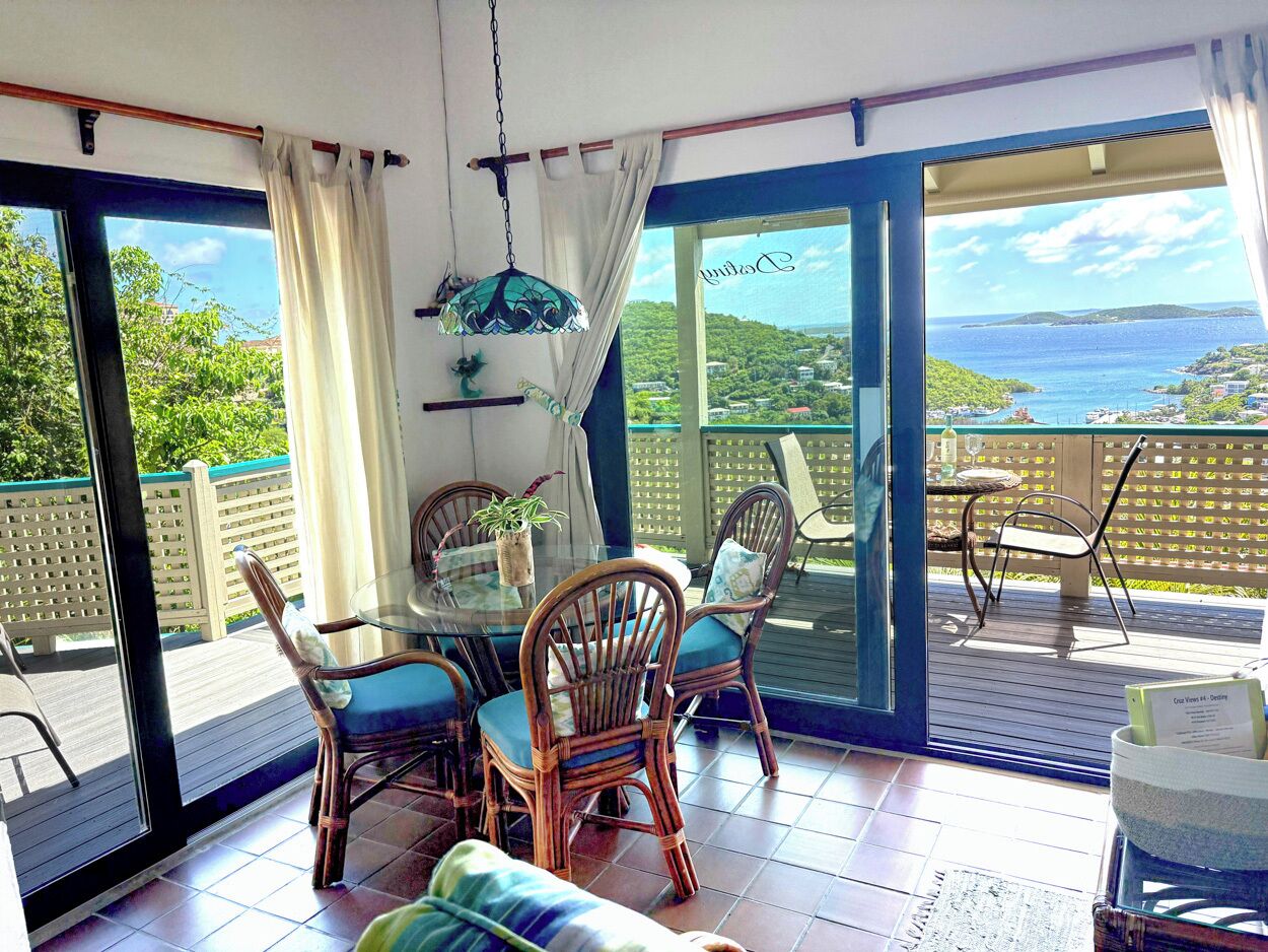 A balcony with a table and chairs, a hanging light fixture, and a view of a coastal landscape.