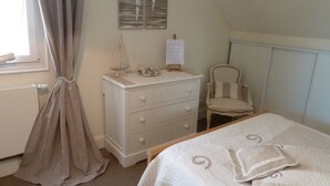 A bedroom with a bed, a dresser, a chair, and a window with curtains. - Chambre d'Hôtes L'Imprevu (Cucq)