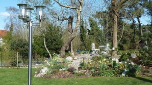 A garden with a metal lamp post, a white bench, and various plants and trees. - Chambre d'Hôtes L'Imprevu (Cucq)