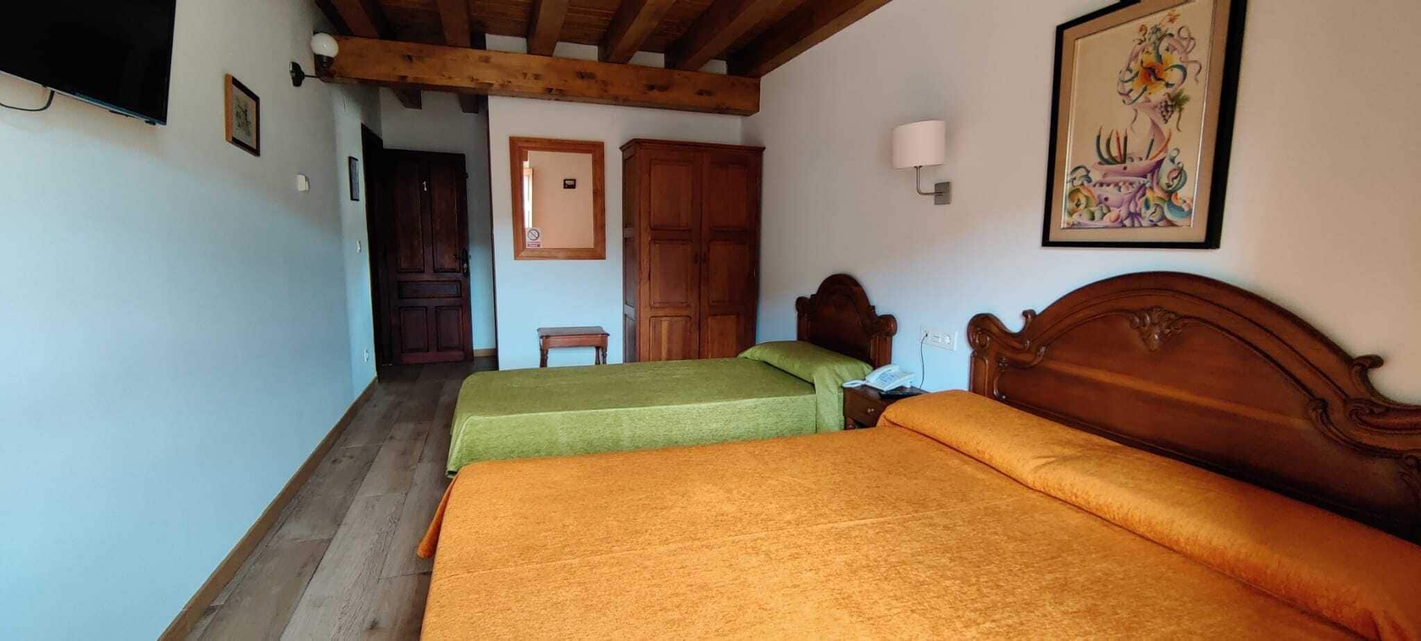 Une chambre avec deux lits, des poutres en bois au plafond, une armoire en bois, un tableau encadré au mur et une petite table avec une lampe.