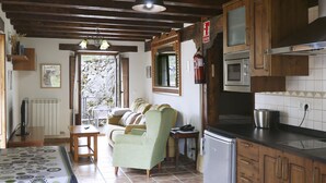 A kitchen with wooden cabinets, a microwave, and a refrigerator. There is a dining table with chairs and a sofa in the adjacent living area. - Hotel Rural La Puebla (Valle de Sedano)