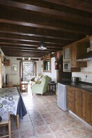 Una cocina con armarios de madera, un microondas y un refrigerador. Hay una mesa de comedor con sillas y un sofá en la zona de estar contigua.