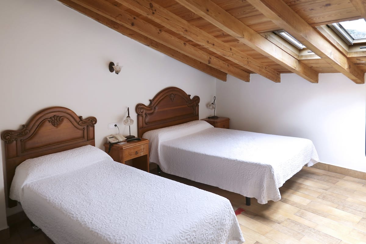 A bedroom with two single beds, wooden headboards, a nightstand with a lamp, and a skylight above.