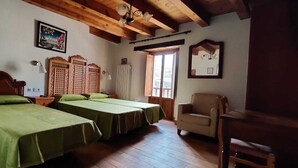 A room with two beds, wooden headboards, a wooden ceiling, a chair, and a window with a view. - Hotel Rural La Puebla (Valle de Sedano)