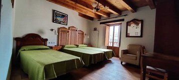 Una habitación con dos camas, cabeceros de madera, techo de madera, una silla y una ventana con vistas.
