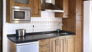 A kitchen with wooden cabinets, a stainless steel microwave, a sink, and a refrigerator. - Hotel Rural La Puebla (Valle de Sedano)