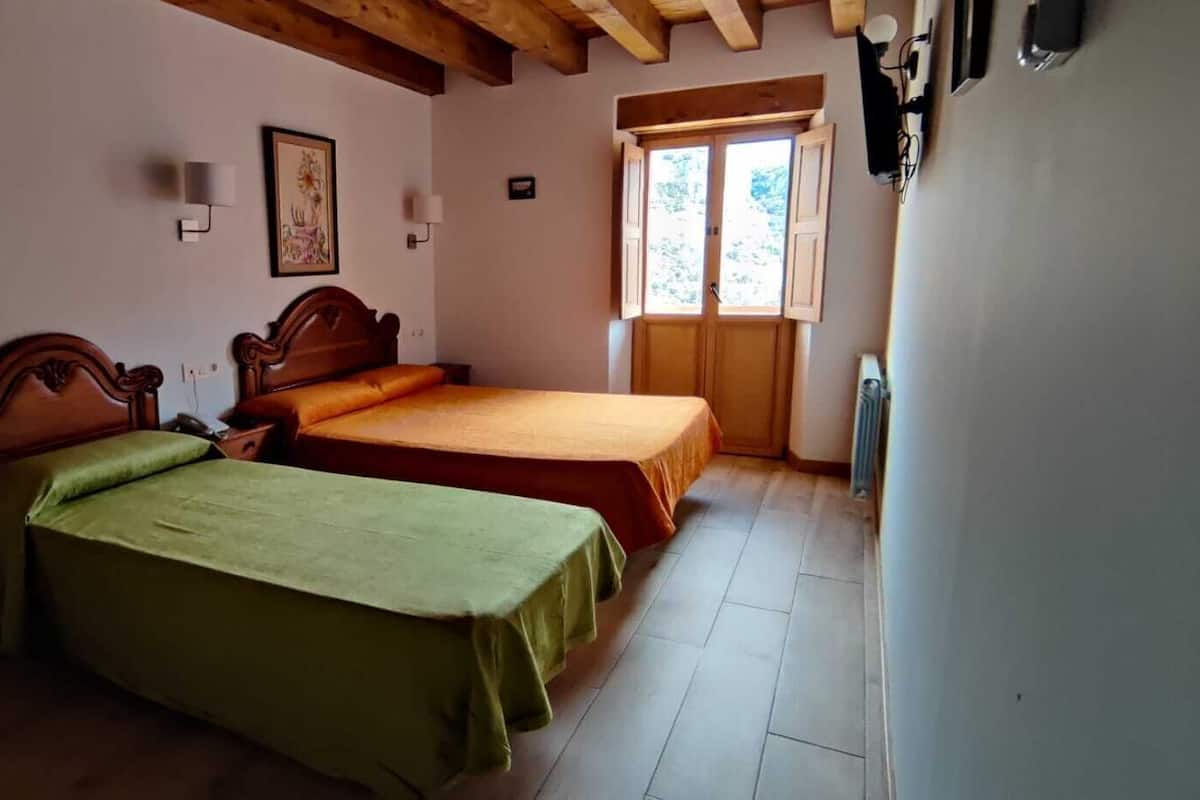 A bedroom with two single beds, wooden headboards, a small window with wooden shutters, and a radiator.