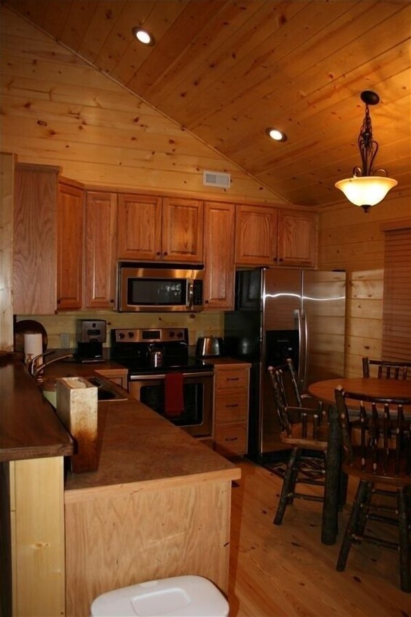 Une cuisine rustique, située dans une cabane en bois, avec un îlot central, des appareils en acier inoxydable et un coin repas doté de chaises en bois.