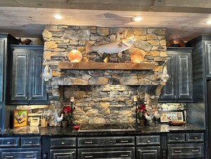Cocina con pared de piedra, estantes de madera y armarios negros.