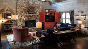 Un salon chaleureux avec une cheminée en pierre, des volets rouges et un coin salon confortable.