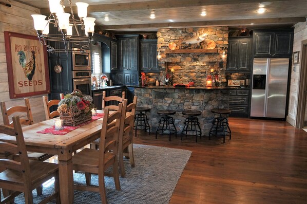 A rustic kitchen with dark cabinets, a stone island, and a stainless steel refrigerator. - ON LAKE BURTON! LAKE HOUSE WITH BOAT DOCK! BOAT AVAILABLE FOR RENT! (Clarkesville)