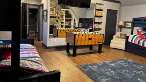 Une chambre confortable avec une table de baby-foot, un lit superposé, une bibliothèque et un téléviseur fixé au mur.