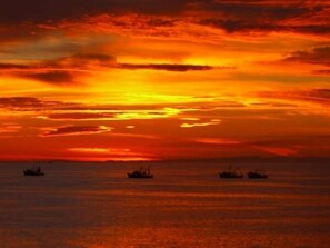 A sunset over the ocean with three ships.
