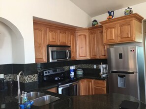 A kitchen with wooden cabinets, a stainless steel refrigerator, a microwave, a stove, and a sink.