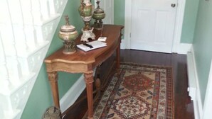 A hallway with a wooden console table, ornate vases, a small statue, and a patterned rug. - Garfield Guest House - Hawksbill Suite (Luray)