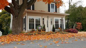 A two-story house with a porch, surrounded by autumn leaves. - Garfield Guest House - Hawksbill Suite (Luray)