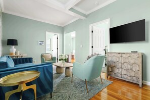 Un salon avec un canapé bleu, une table basse ronde, un fauteuil turquoise et un meuble en bois orné d’un motif géométrique.