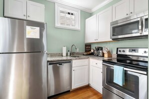 A modern kitchen with stainless steel appliances, white cabinetry, and a granite countertop.
