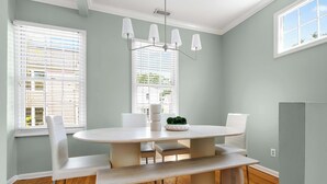 A dining area with a round table, white chairs, a bench, and a potted plant.