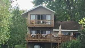 Een houten huis met twee verdiepingen, met een balkon op de bovenverdieping en een overdekte veranda beneden.