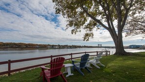 A riverside view with a wooden fence, a large tree, and Adirondack chairs. - Oceanfront Home Great For Families! Near Amenities, Canal, & More! (Buzzards Bay)