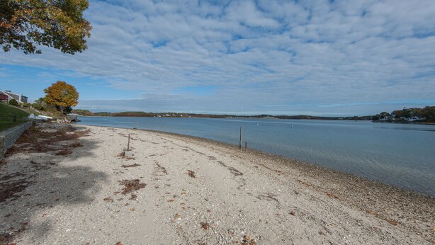 A beach with a sandy shore, a grassy area, and a body of water in the background. - Oceanfront Home Great For Families! Near Amenities, Canal, & More! (Buzzards Bay)