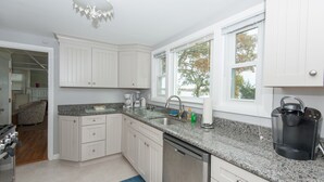 A modern kitchen with white cabinetry, granite countertops, a built-in dishwasher, and a coffee maker. - Oceanfront Home Great For Families! Near Amenities, Canal, & More! (Buzzards Bay)