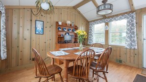 A wooden dining room with a table set for four, surrounded by chairs. A vase with yellow flowers is on the table. - Oceanfront Home Great For Families! Near Amenities, Canal, & More! (Buzzards Bay)