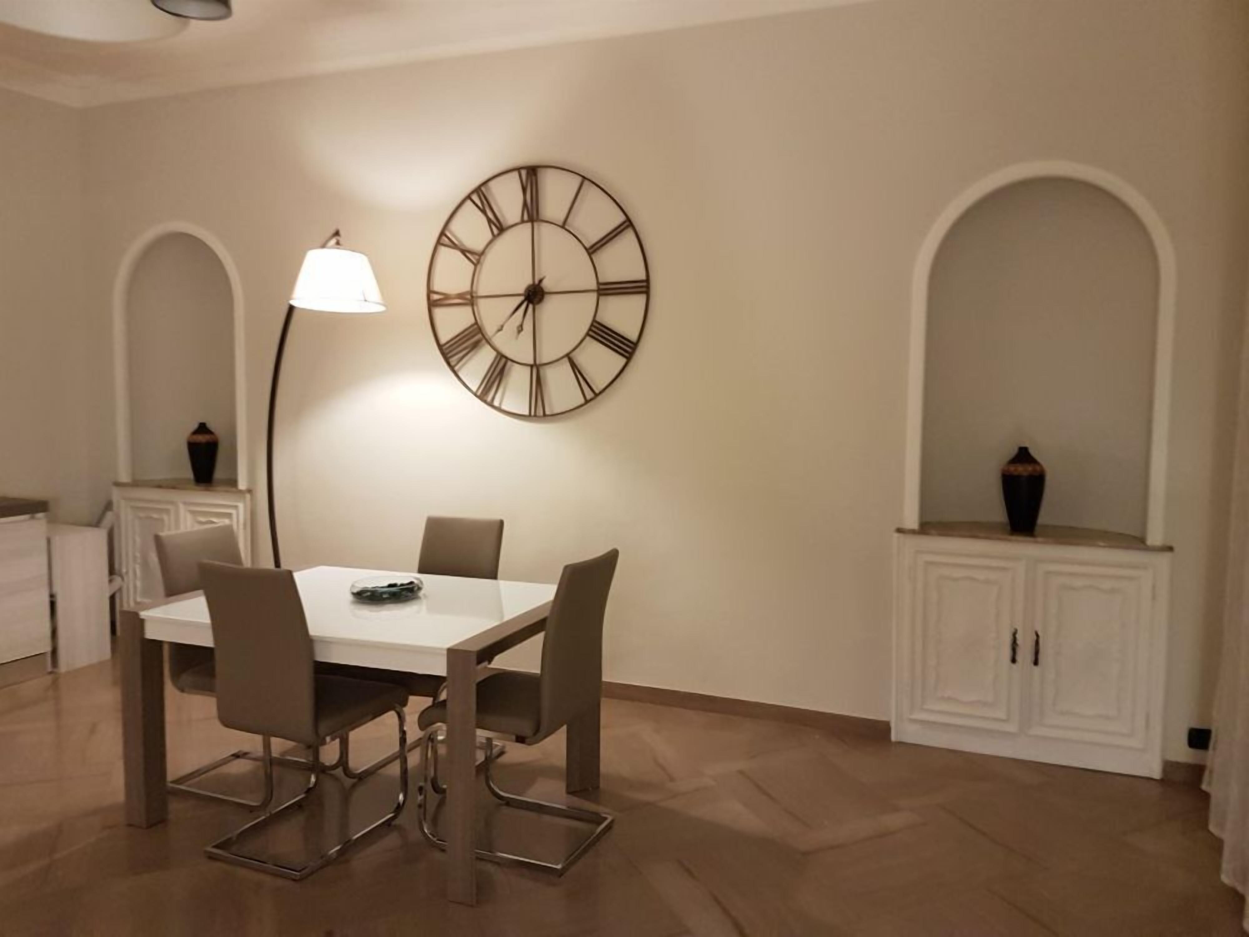 Un espace repas comprenant une table, des chaises, une horloge murale, une lampe et des placards.