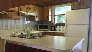 Eine Küche mit Holzausstattung, einer weißen Arbeitsplatte, einem Edelstahlspülbecken, einer Mikrowelle, einer Kaffeemaschine und einem Kühlschrank.