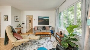 Een woonkamer met een bank, fauteuil, salontafel en een groot raam met gordijnen.