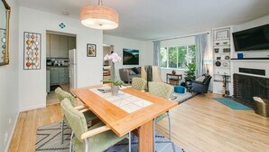 Een moderne woonkamer met een houten eettafel, groene stoelen, een open haard en een televisie.