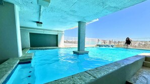 Une piscine avec une eau d’un bleu limpide, une balustrade blanche et une personne à l’arrière-plan.