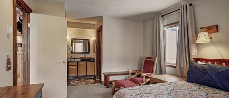 Un dormitorio con cama, escritorio, silla, espejo y ventana con cortinas.