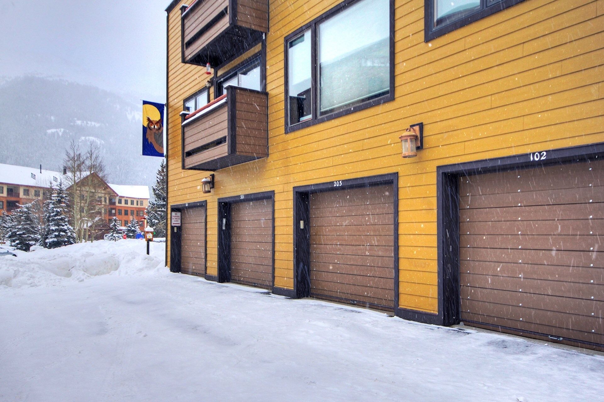 Un bâtiment jaune doté de plusieurs portes de garage, numérotées 201 et 203, et d’un balcon offrant une vue sur le paysage enneigé.