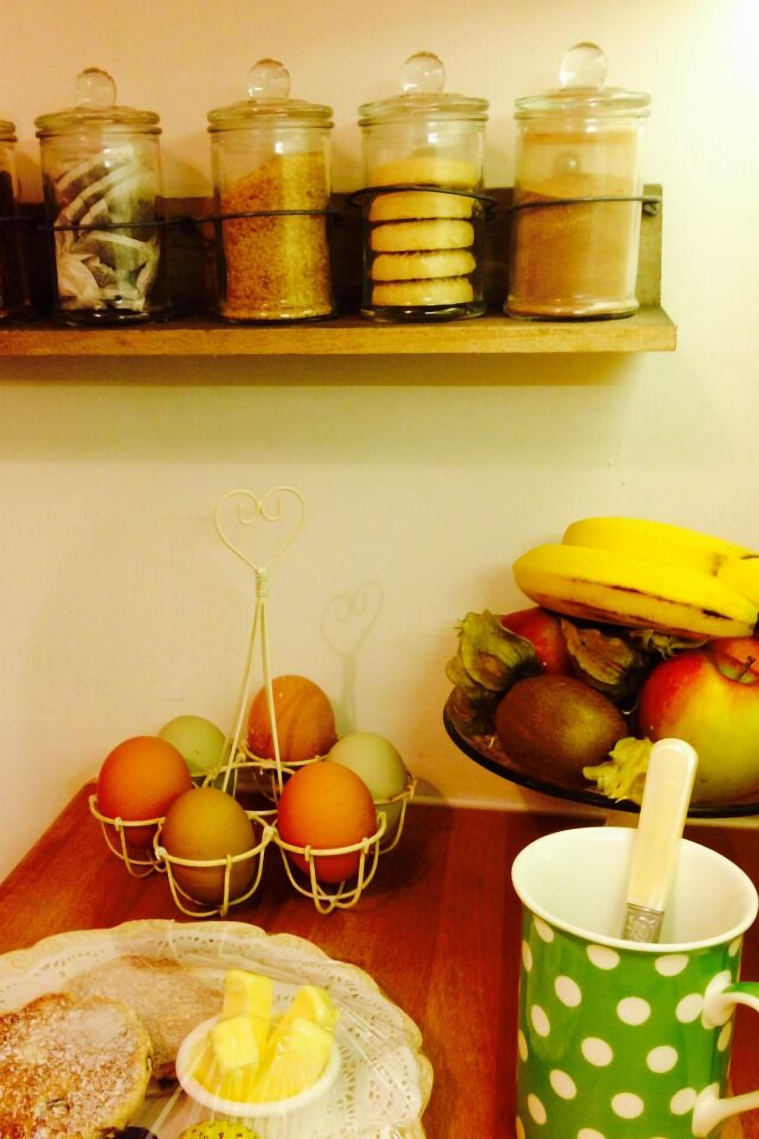 A kitchen counter with jars of spices, a fruit bowl, a polka-dotted mug, and a basket of eggs.