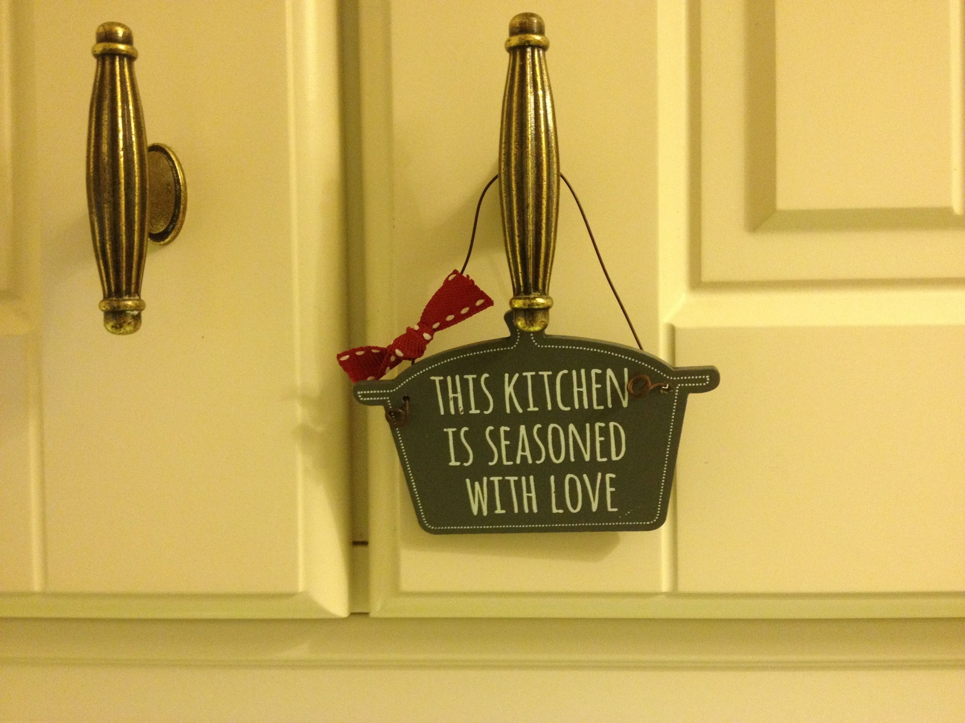A kitchen sign with the text "THIS KITCHEN IS SEASONED WITH LOVE" hanging on a door.