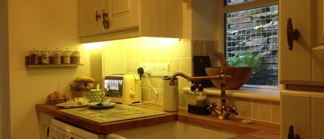 A kitchen with a washing machine, a wooden countertop, a window with a view, and a shelf with jars.
