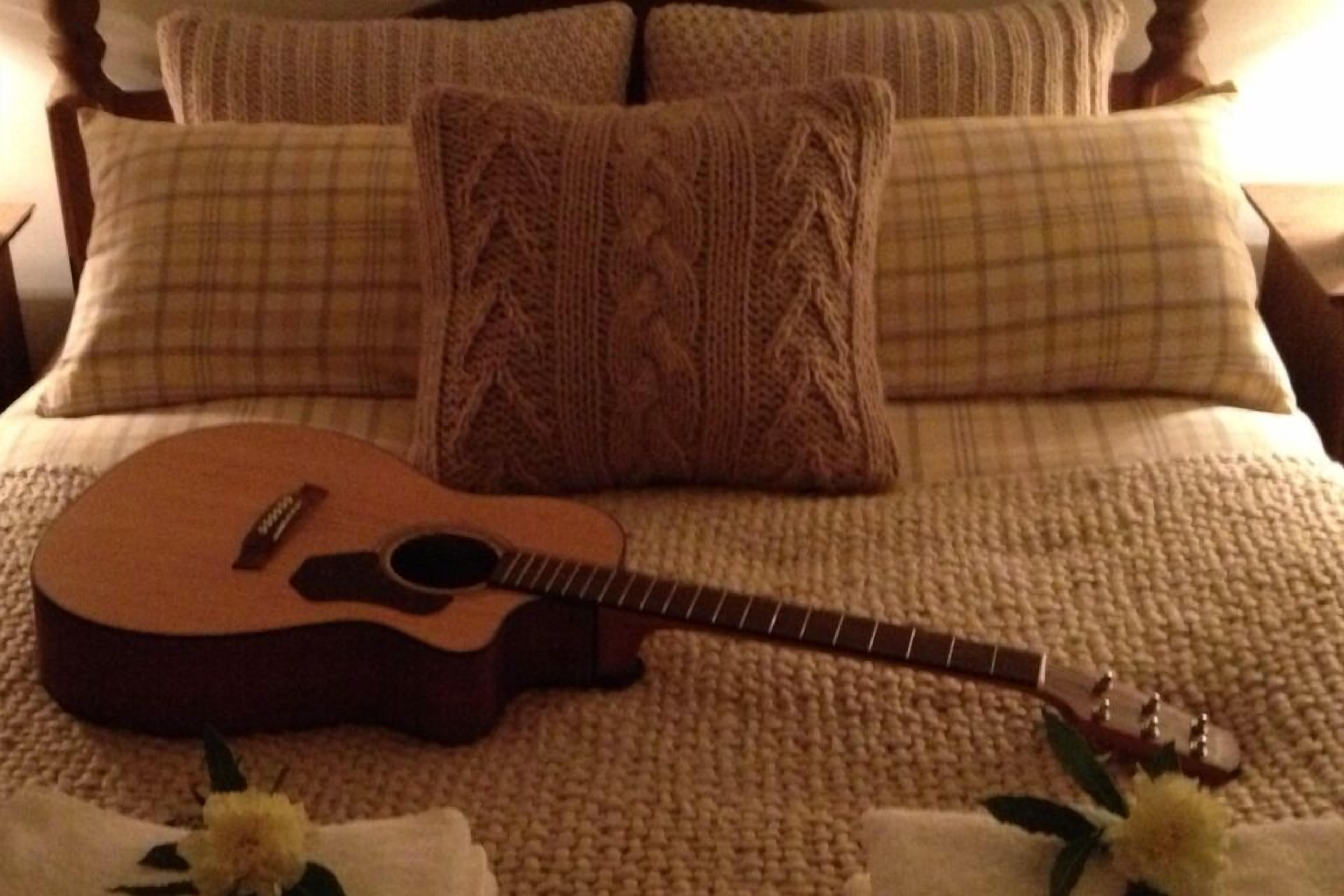 Una cama con una guitarra, almohadas y una colcha.