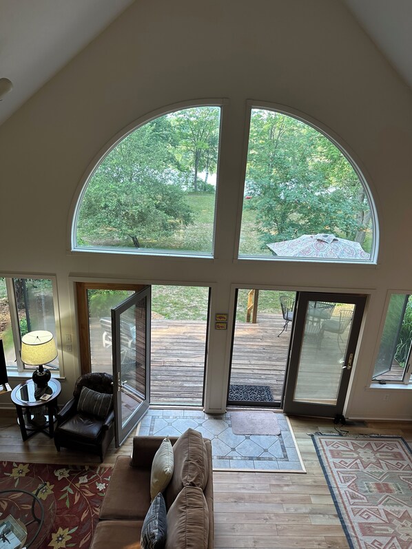 A spacious living room with a high ceiling, large arched windows, a leather sofa, a coffee table, and a lamp.