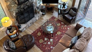 Un salon spacieux doté d’une cheminée en pierre, d’un téléviseur à écran plat, de canapés en cuir et d’une grande fenêtre offrant une vue sur l’extérieur.