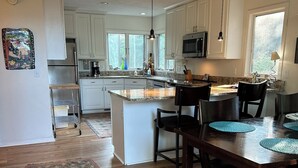 Une cuisine moderne avec des meubles blancs, un îlot central et un coin repas doté de chaises en bois foncé.