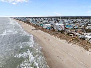 A coastal town with beachfront properties, a pier, and a large hotel with a distinctive red and white design. - Sol Shine - Dog Friendly, Oceanfront House, Large Deck,Private Beach Access! (Carolina Beach)