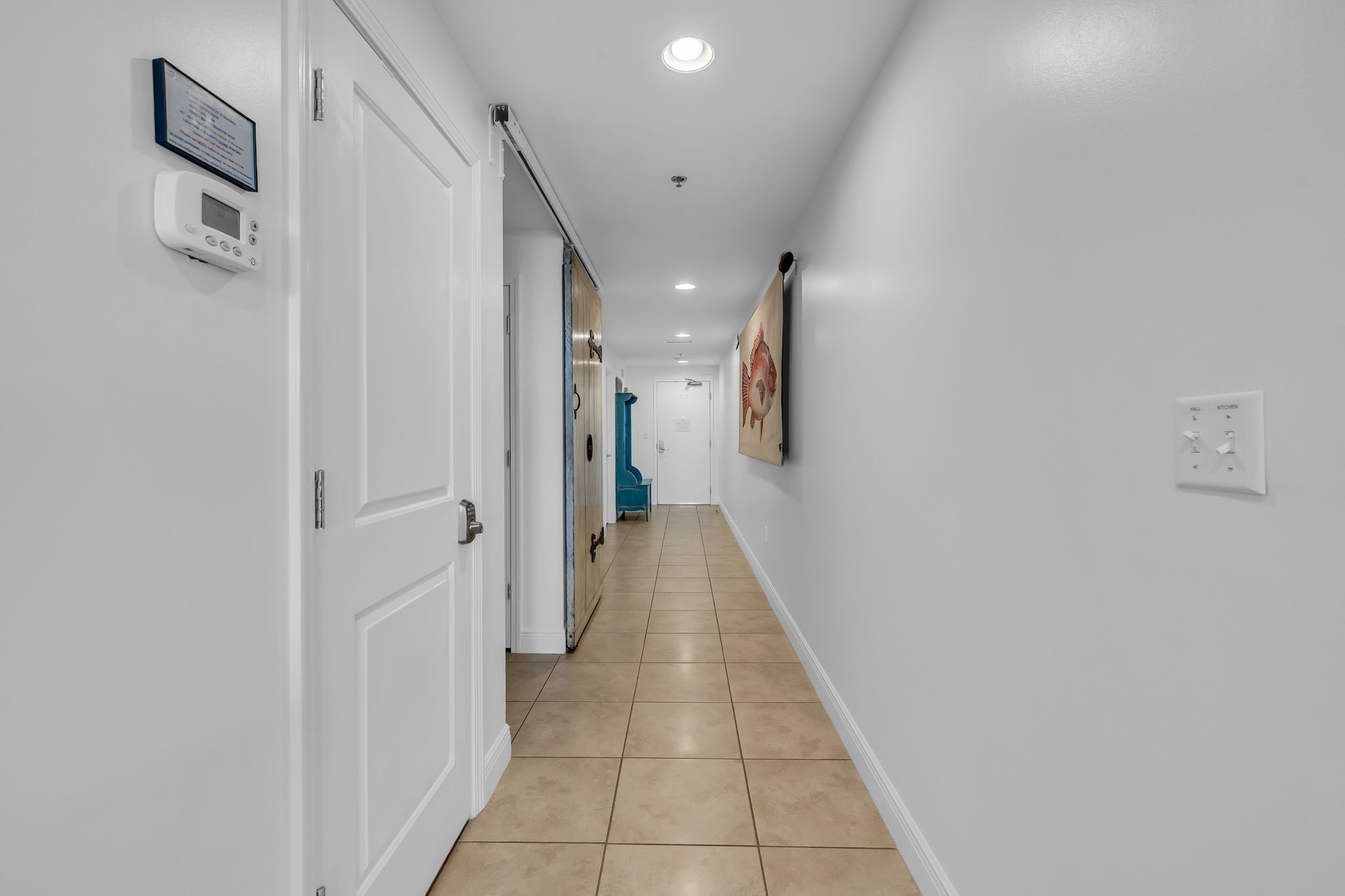 A hallway with white walls, a tiled floor, and a door on the left.