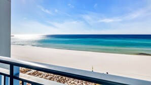 Vista a la playa desde un balcón con barandilla, cielo despejado y mar en calma.