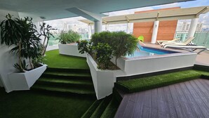Een dakterras met kunstgras, een zwembad en ligbedden.