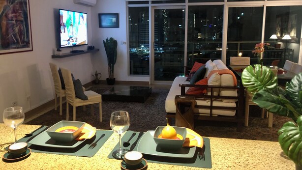 Een moderne woonkamer met een televisie, zitplaatsen en een eethoek voor twee personen.