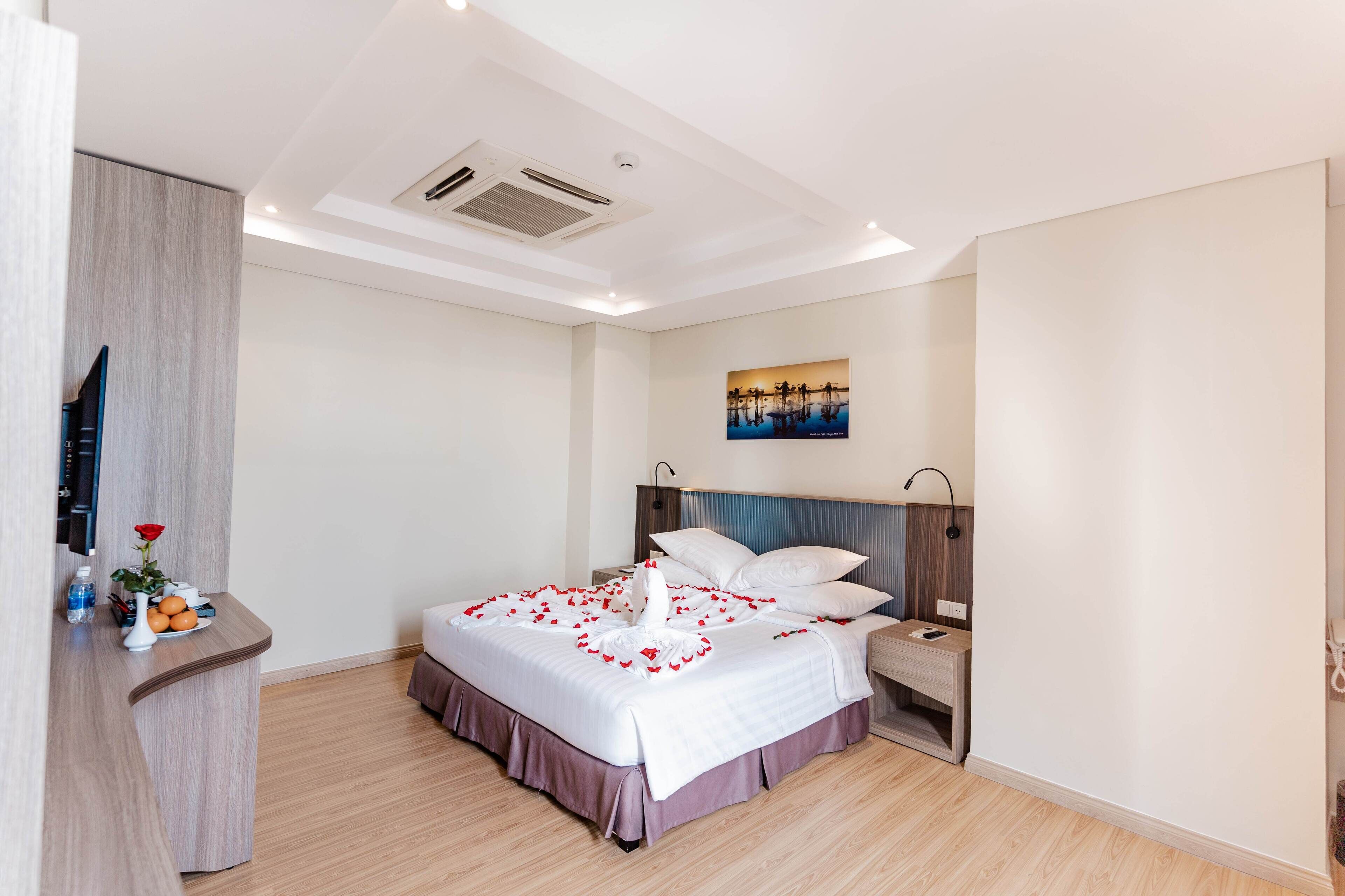 A modern hotel room with a neatly made bed, a bedside table with a lamp, and a painting on the wall.